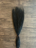 Black synthetic fishing lure material with subtle sparkle strands laid out on a wooden surface, designed for use with Squimpish Sparkle Blend fishing tackle.
