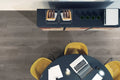 overhead view of office with dark colored flooring, round black table with 3 yellow chairs, and file cabinet