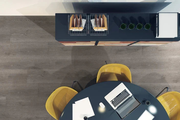 overhead view of office with dark colored flooring, round black table with 3 yellow chairs, and file cabinet